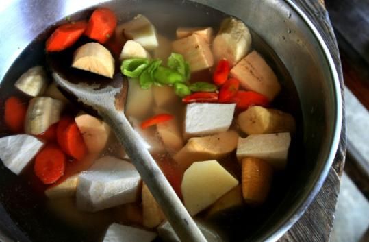 a pot filled with lots of food on top of a wooden table next to a spoon