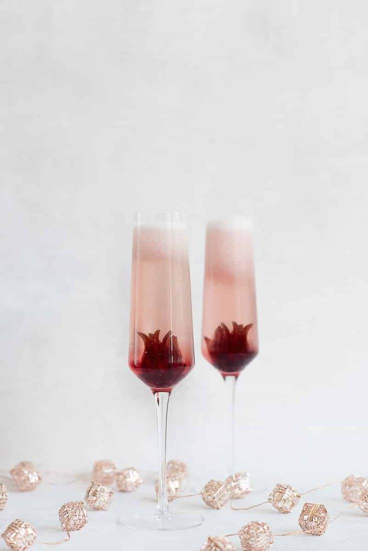 two wine glasses filled with pink liquid and garnished with rose petals on a white surface