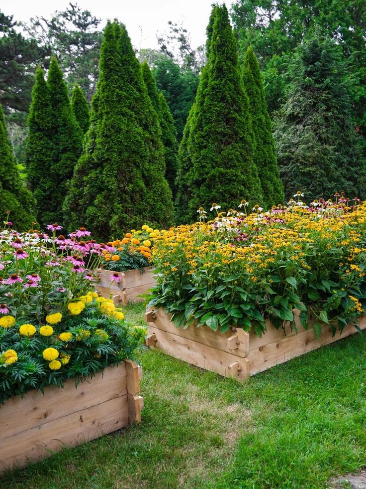 several wooden planters filled with flowers in the middle of some grass and trees behind them