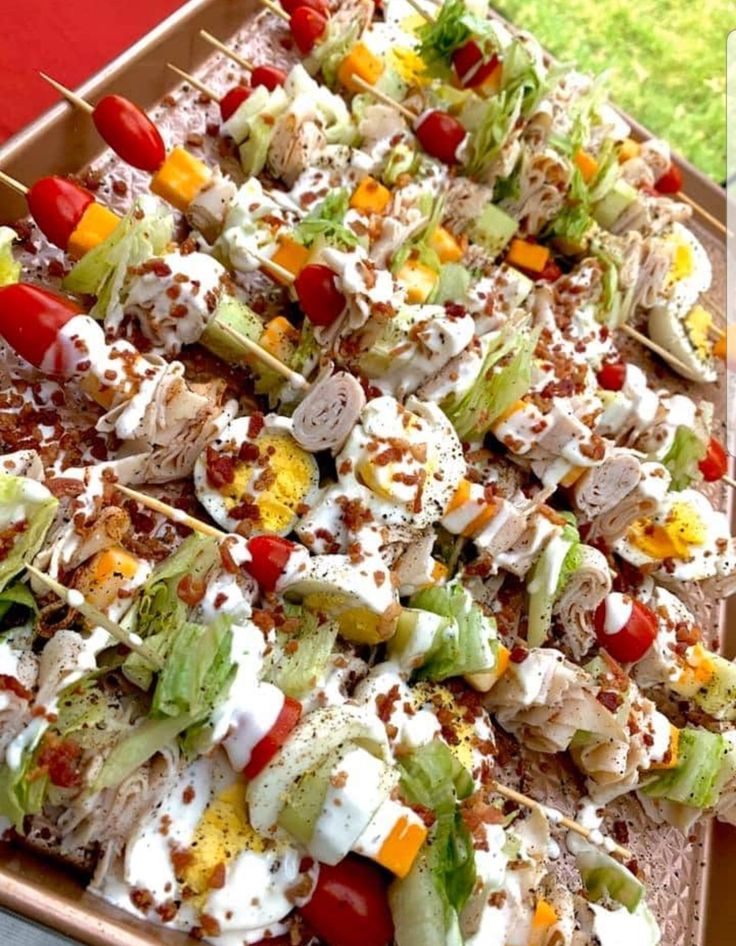 a tray filled with lots of different types of food on skewers next to a red table