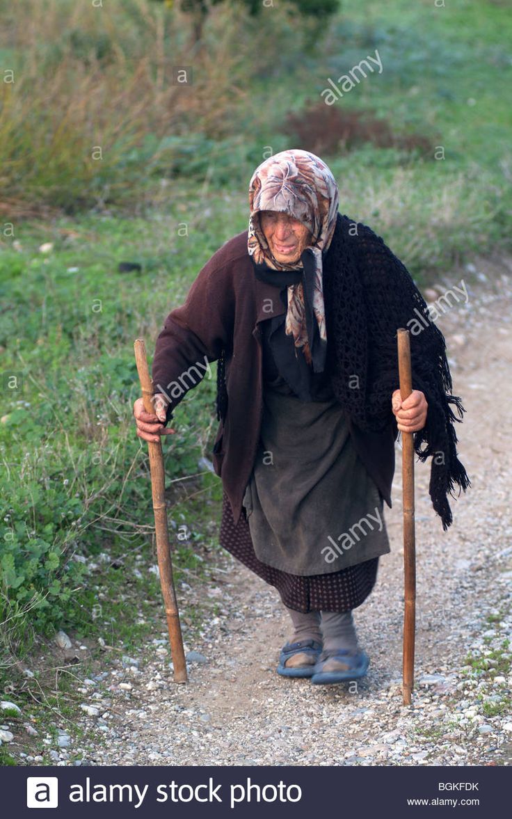 an old woman walking down a dirt road carrying two wooden poles