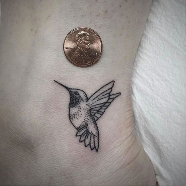 a small hummingbird tattoo on the side of a woman's right leg, next to a penny