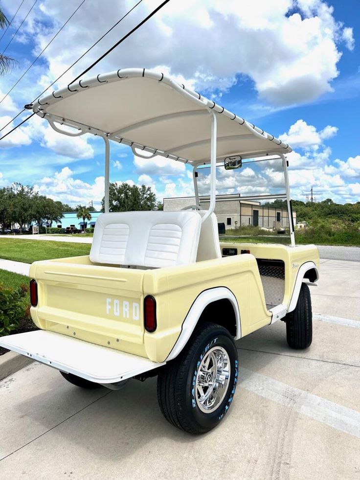 a yellow four passenger golf cart parked in a parking lot next to a palm tree