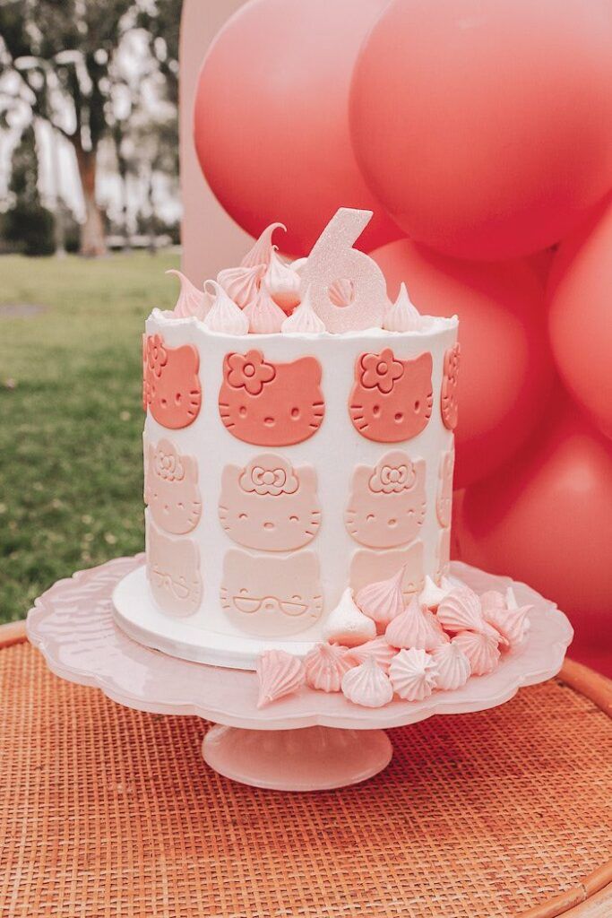 a hello kitty cake on a table with balloons in the background