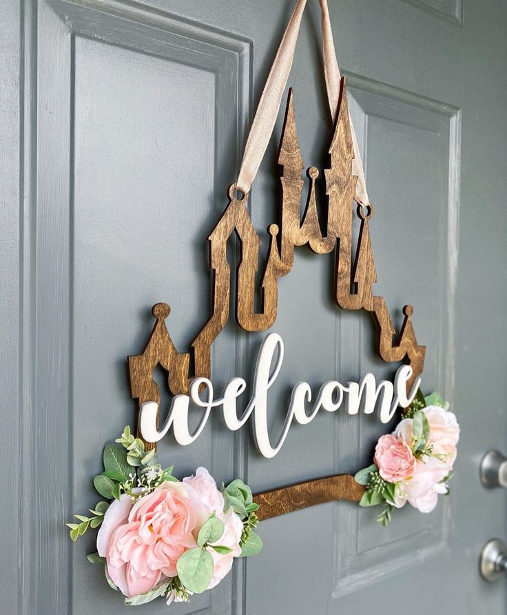 a welcome sign hanging on the front door with pink flowers and greenery around it