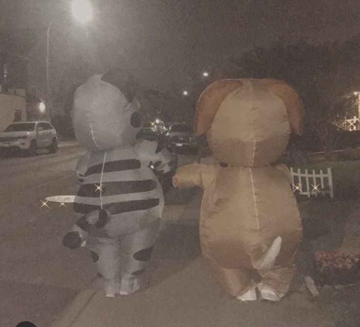 two inflatable elephants are walking down the street at night, one is wearing a black and white striped shirt