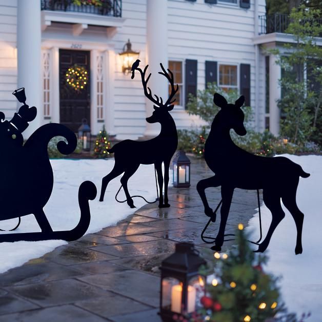 three metal reindeers with sleigh in front of a white house at christmas time