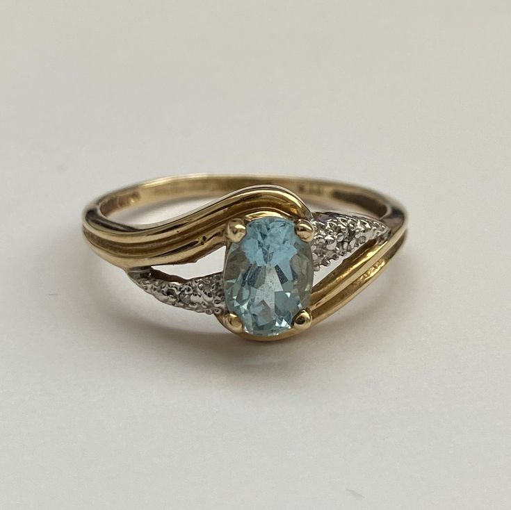 an oval blue topaz ring with two white diamonds on the sides and a yellow gold band