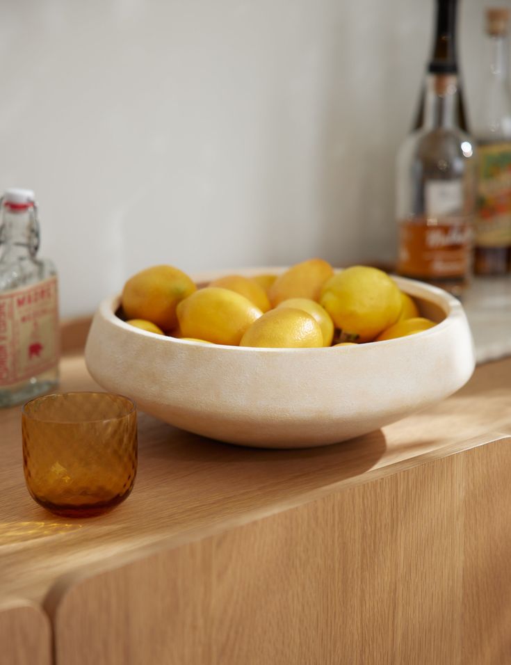 a bowl full of lemons sitting on top of a wooden counter next to bottles