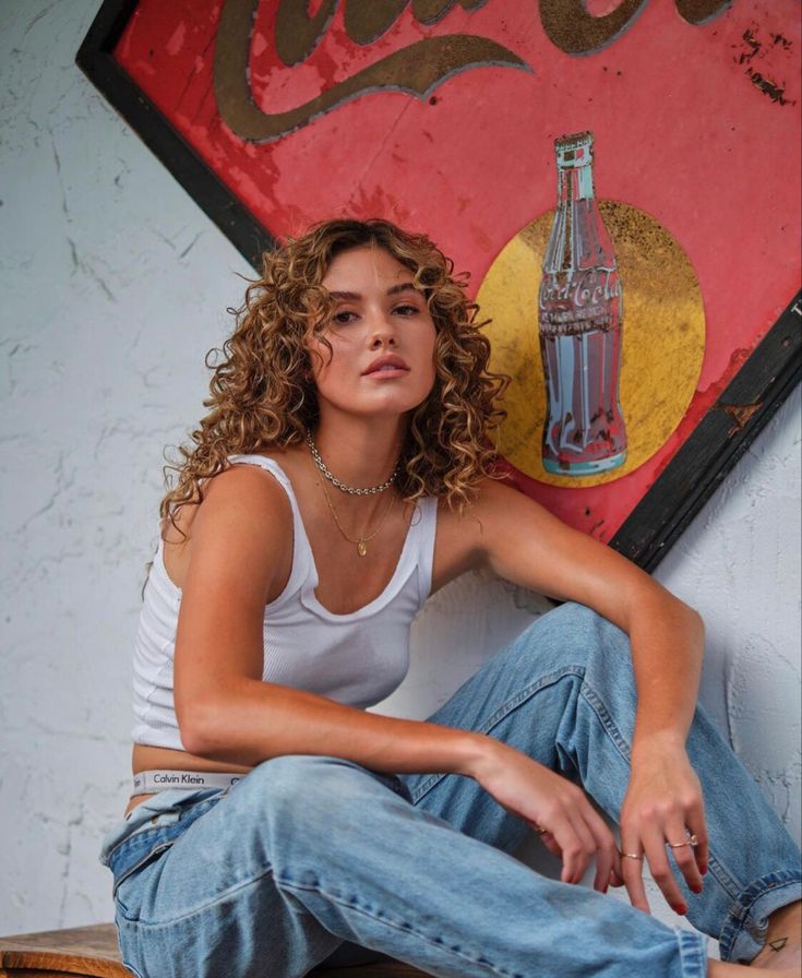 a woman sitting on top of a stool next to a coca - cola sign and bottle