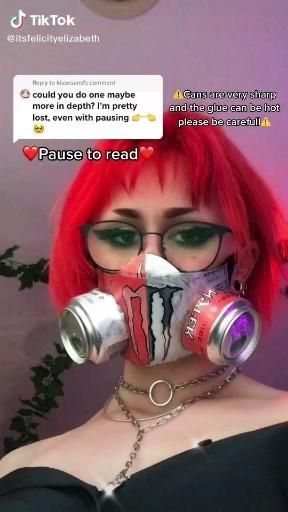 a woman with red hair wearing a gas mask and holding two cans in her mouth