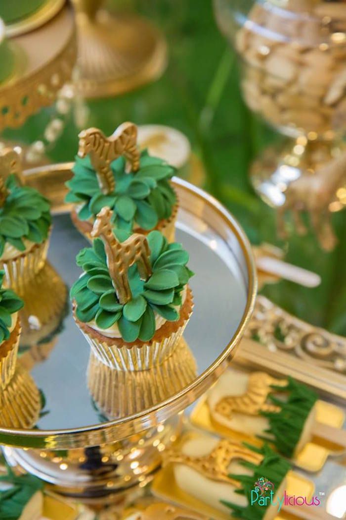 cupcakes with green frosting and gold decorations on a tray at a party