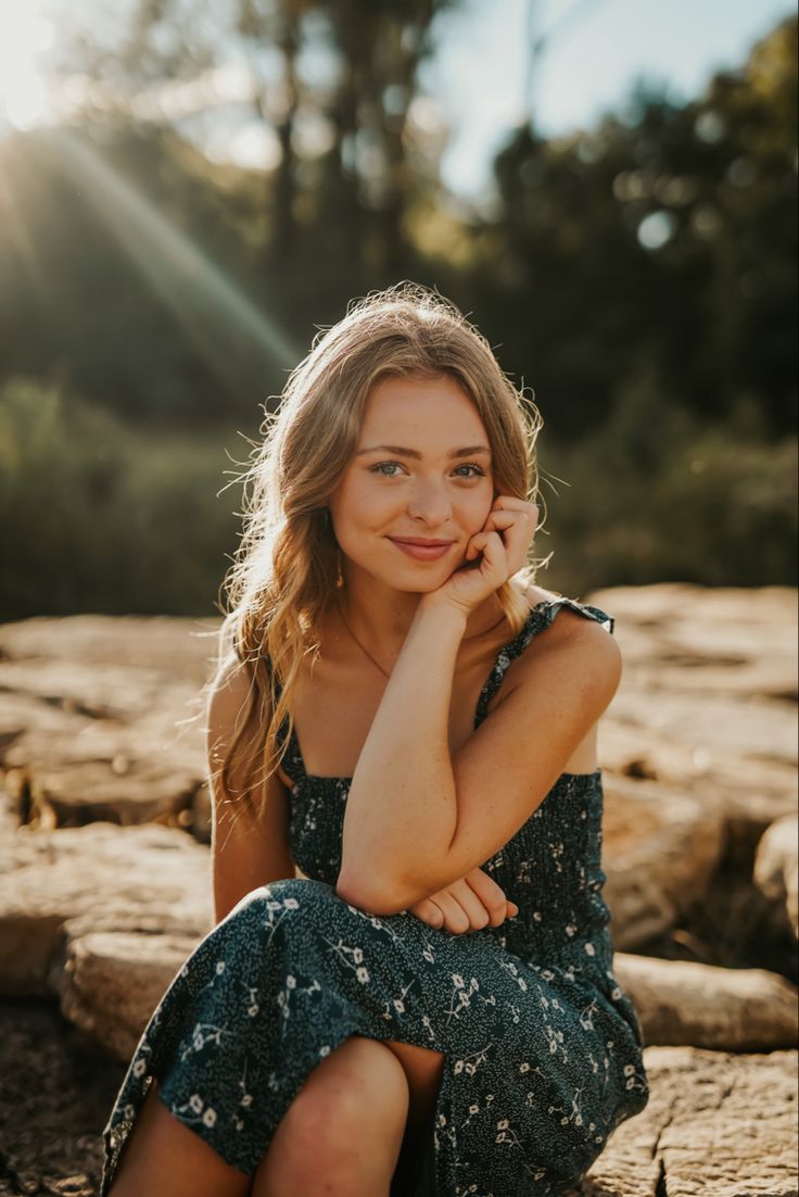 a beautiful young woman sitting on top of a rock next to a tree trunk in the sun