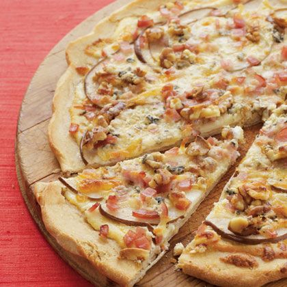 a pizza with several toppings cut into slices on a wooden cutting board next to a red table cloth