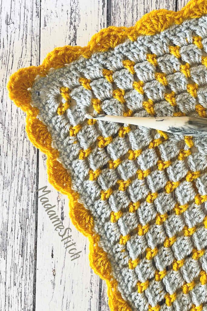 a crocheted dishcloth with yellow and gray squares on it next to a pair of scissors