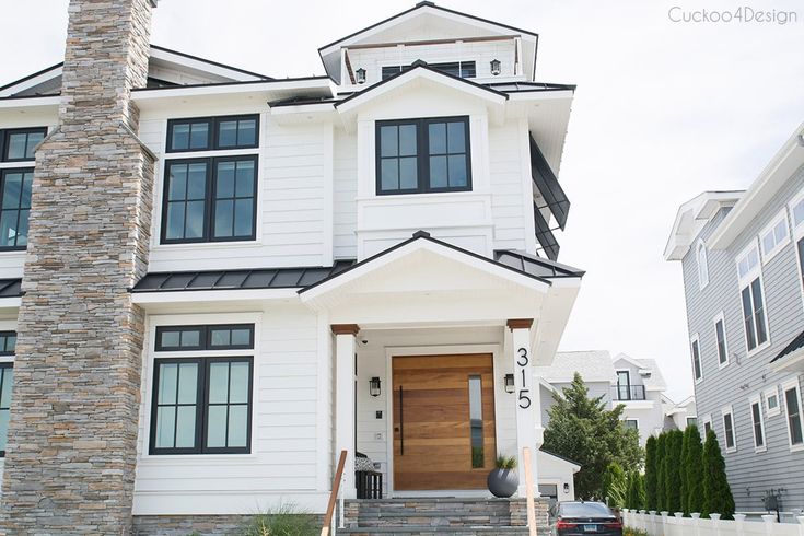 a white two story house with black trim and wood front door on a street corner