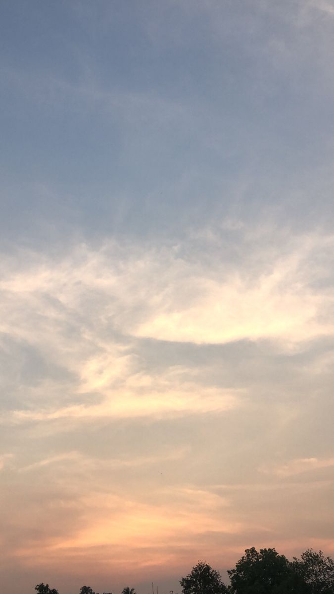 the sky is filled with clouds and some trees in the foreground as the sun sets