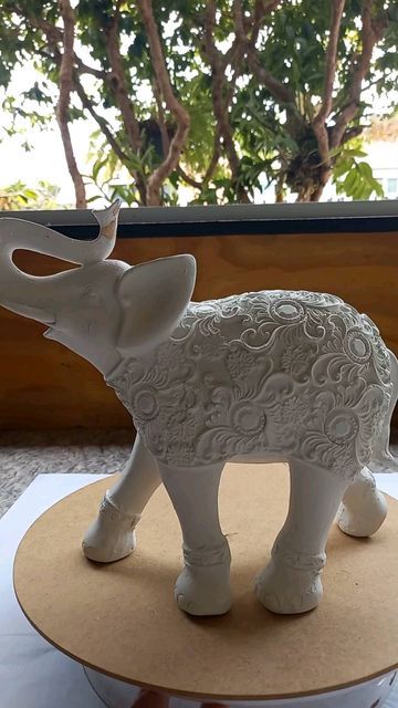 a white elephant figurine sitting on top of a wooden table next to a window