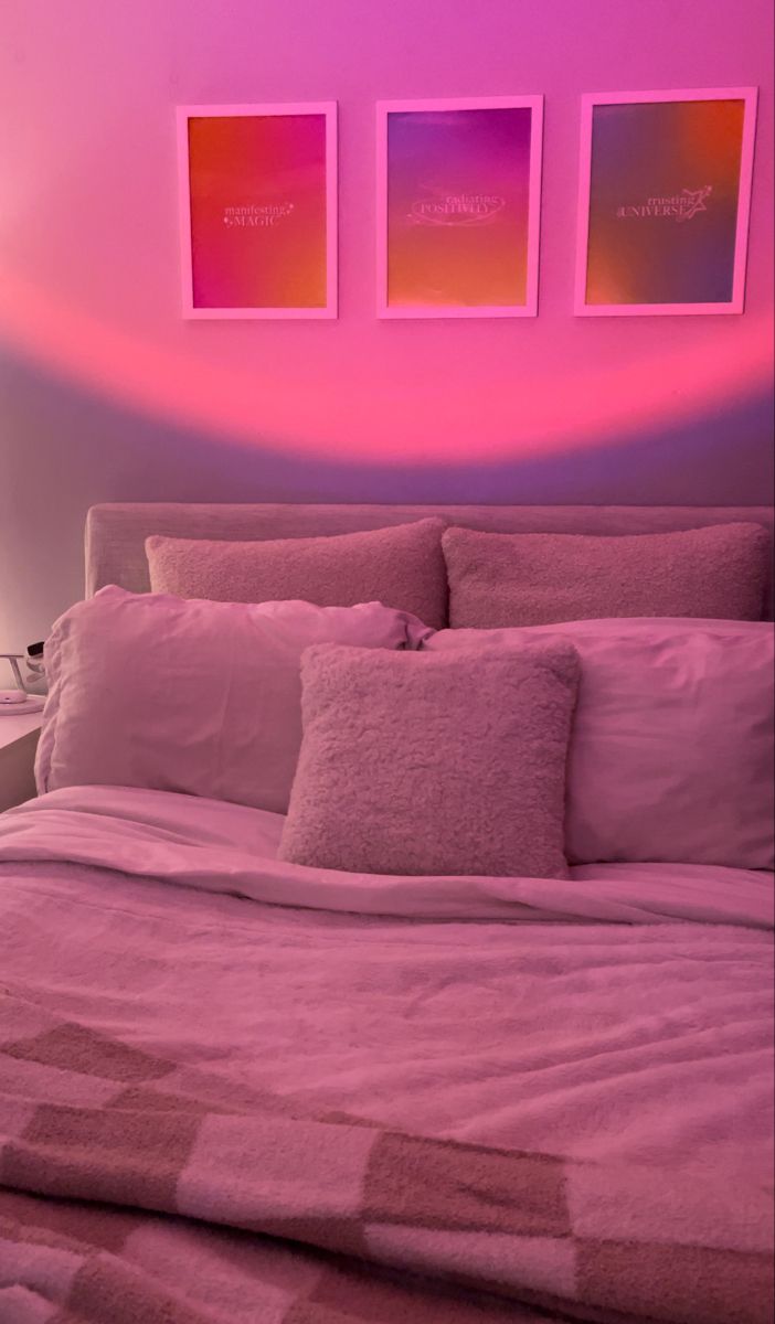 a bed with pink sheets and pillows in a room that has three pictures on the wall