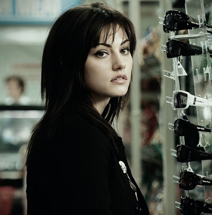 a woman standing in front of a rack of glasses and looking at the camera with an intense look on her face