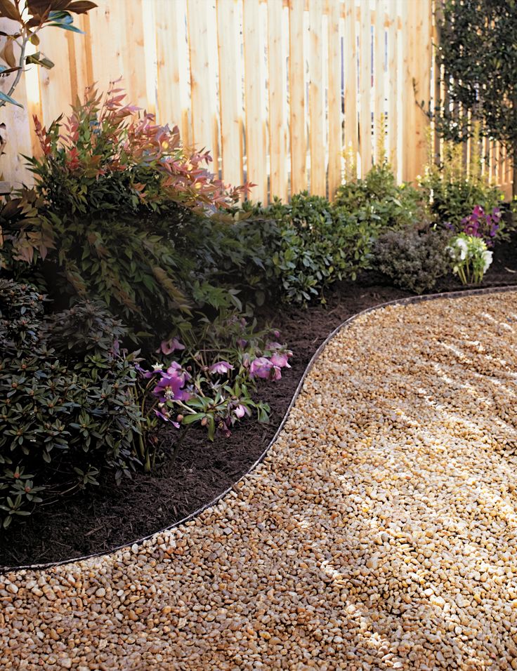 a garden area with gravel and flowers in the foreground, next to a wooden fence