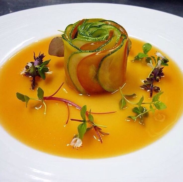 a white plate topped with a cucumber and orange sauce covered in green leafy garnish