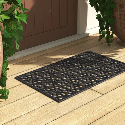 a black door mat sitting on top of a wooden floor next to potted plants