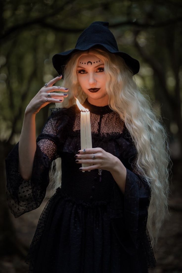 a woman with long blonde hair holding a candle in her hands and wearing a witches costume