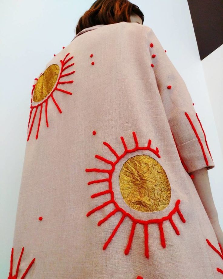 a woman is wearing a pink coat with red trims and gold sun designs on it