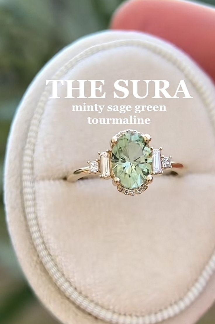 an engagement ring with a green stone surrounded by three baguets and the words, the sura minty sage green tourmaline