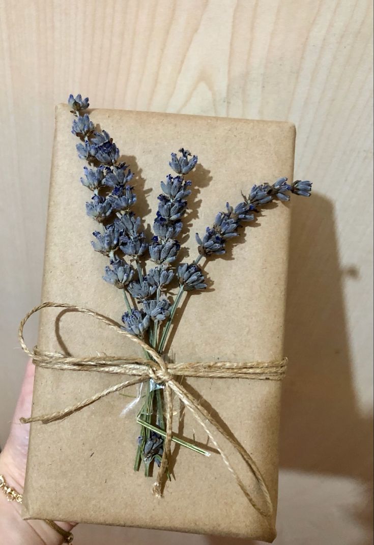 a hand holding a wrapped gift with lavender flowers tied around the wrap and string on it