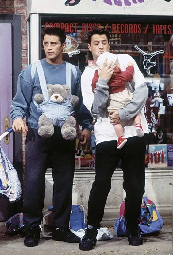 two men standing in front of a store holding their baby and teddy bear while another man holds the infant