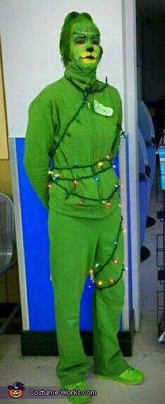 a man dressed in green is standing next to a wall with christmas lights on it