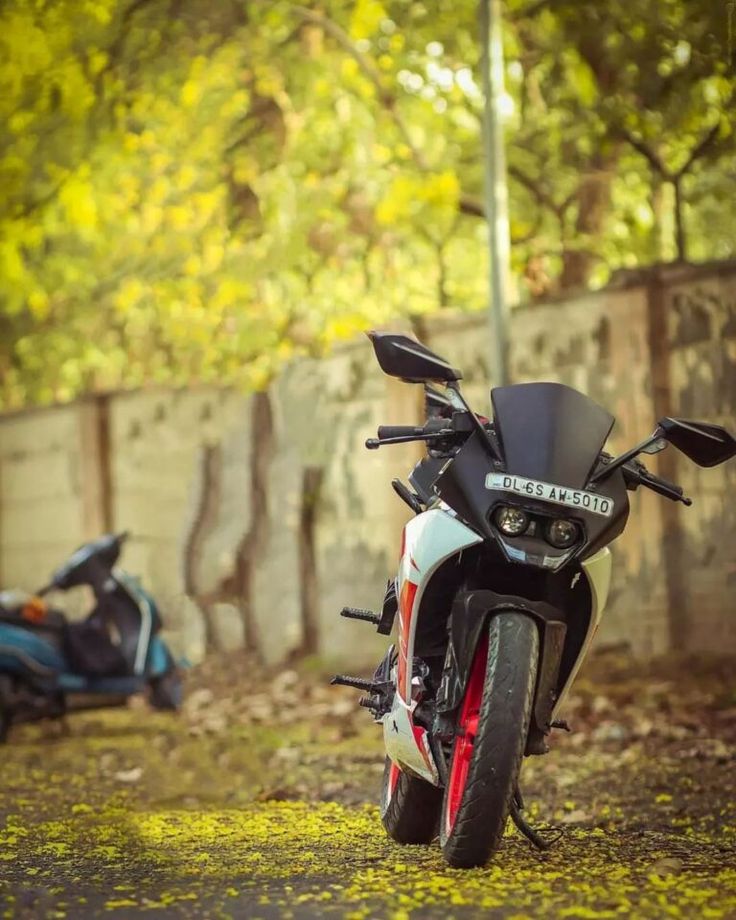 a motorcycle parked on the side of a road next to a tree filled street with yellow leaves