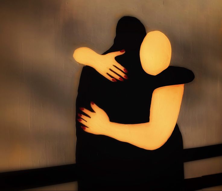 two people hugging each other in front of a gray wall with orange lights on it