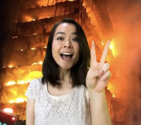 a woman holding up her peace sign in front of a building that is on fire