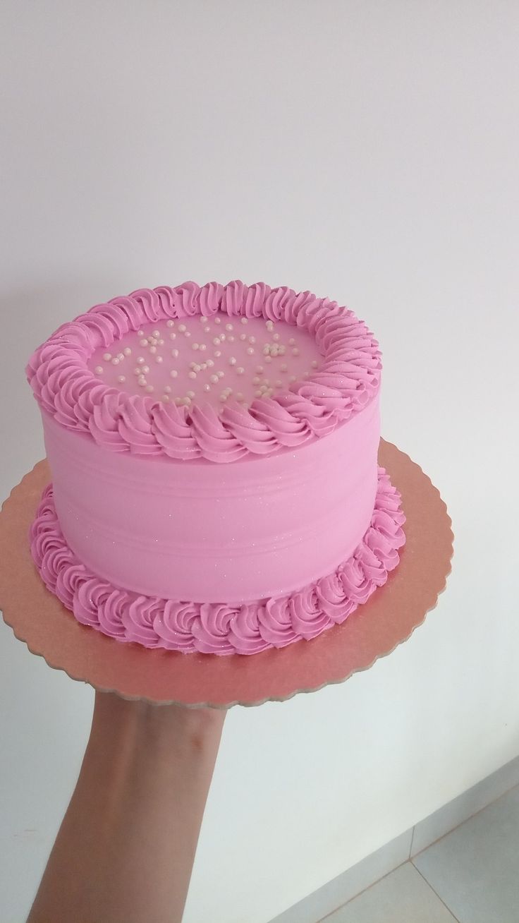 a pink cake sitting on top of a wooden plate next to a person's hand