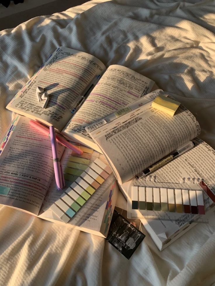 there are many books on the bed with pens and pencils next to each other