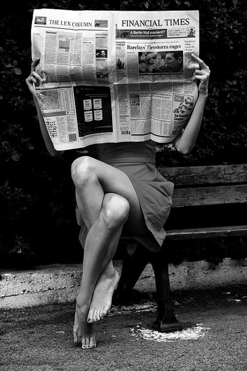 a woman is sitting on a bench reading the financial times newspaper with her legs crossed