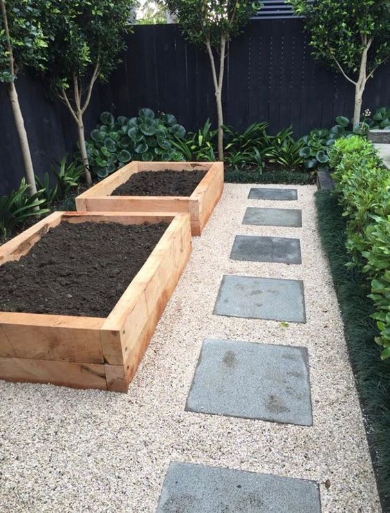 an outdoor garden with several wooden planters filled with dirt and plants in the middle