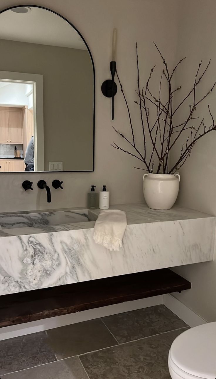 a bathroom with a marble counter top next to a white toilet and mirror above it