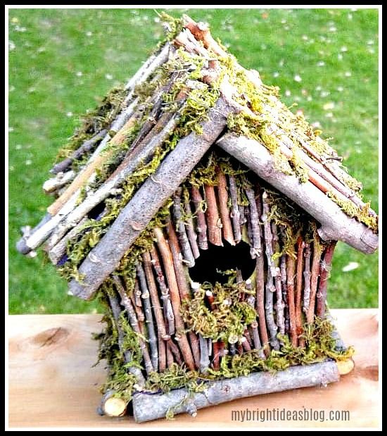 a birdhouse made out of sticks and grass with a black cat in the hole