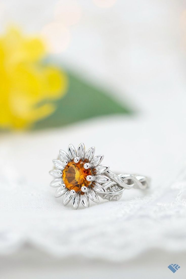 a close up of a ring with a flower on the front and an orange stone in the middle