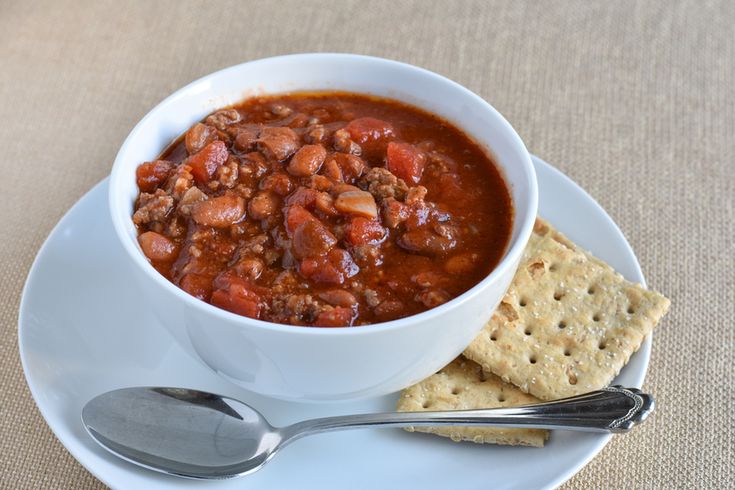 a white plate topped with a bowl of chili and crackers