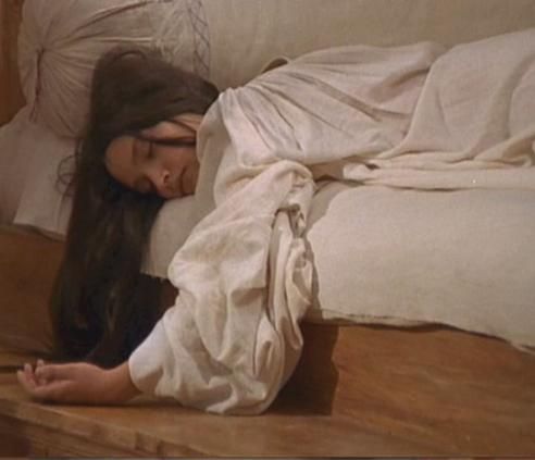 a woman laying on the floor with her head in her hands and eyes closed, next to an unmade bed