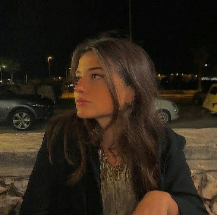 a woman sitting on a stone wall looking off into the distance with cars in the background