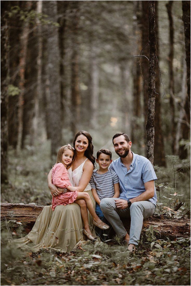 a family sitting on a log in the woods with their two children and one adult