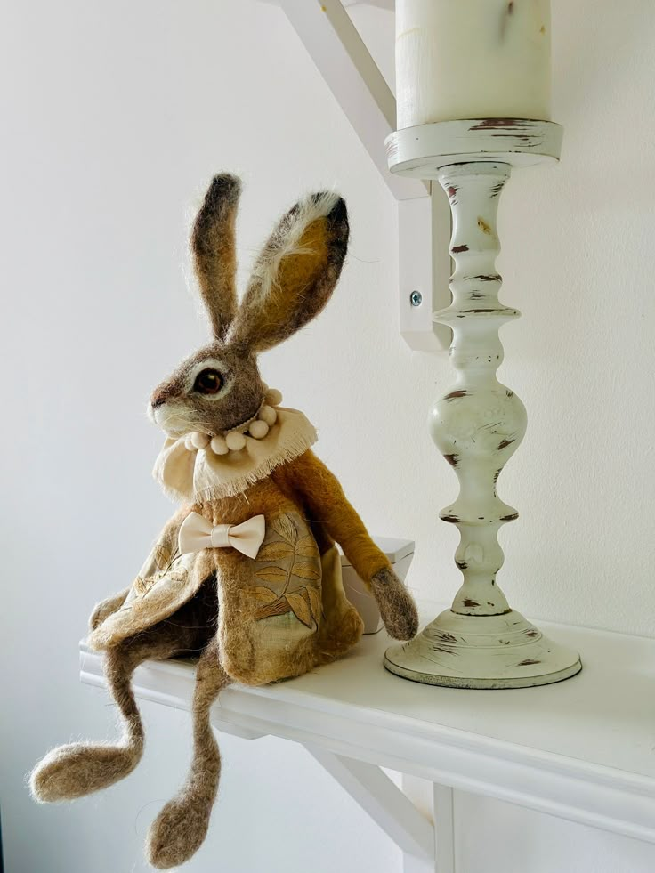 a stuffed rabbit sitting on top of a white shelf next to a candelabra