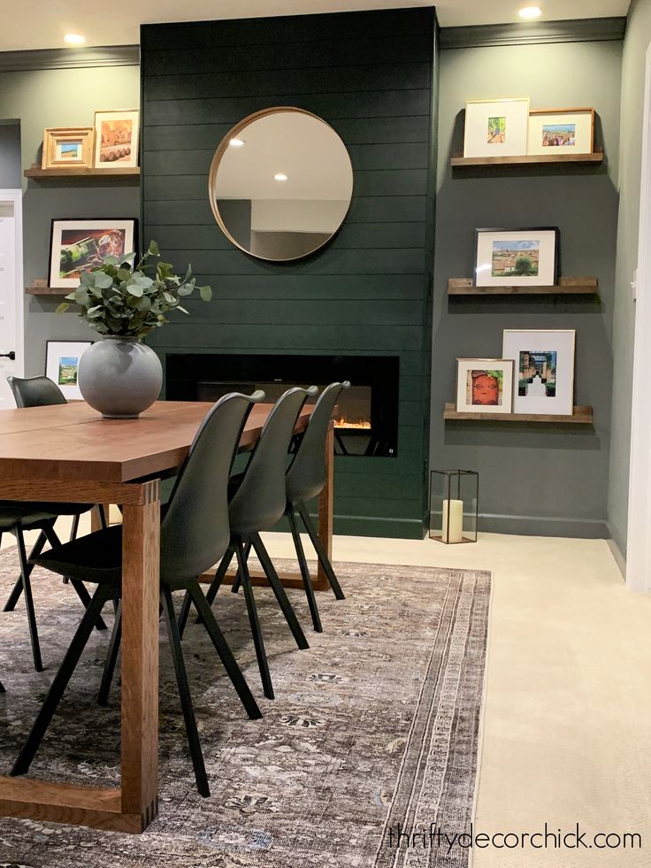 a dining room table with chairs and a round mirror on the wall above it in front of a fireplace