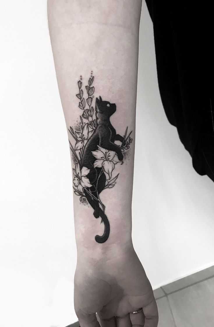 a person with a tattoo on their arm holding a black cat and white flowers in the background